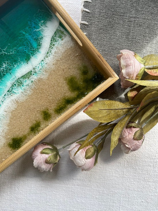 Resin art serving tray featuring a bamboo base, adorned with sea shells and sand, encapsulated in ocean wave designs created with resin.