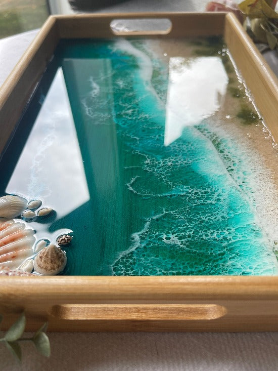 Resin art serving tray featuring a bamboo base, adorned with sea shells and sand, encapsulated in ocean wave designs created with resin.