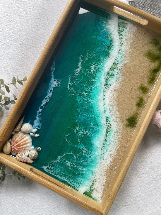 Resin art serving tray featuring a bamboo base, adorned with sea shells and sand, encapsulated in ocean wave designs created with resin.