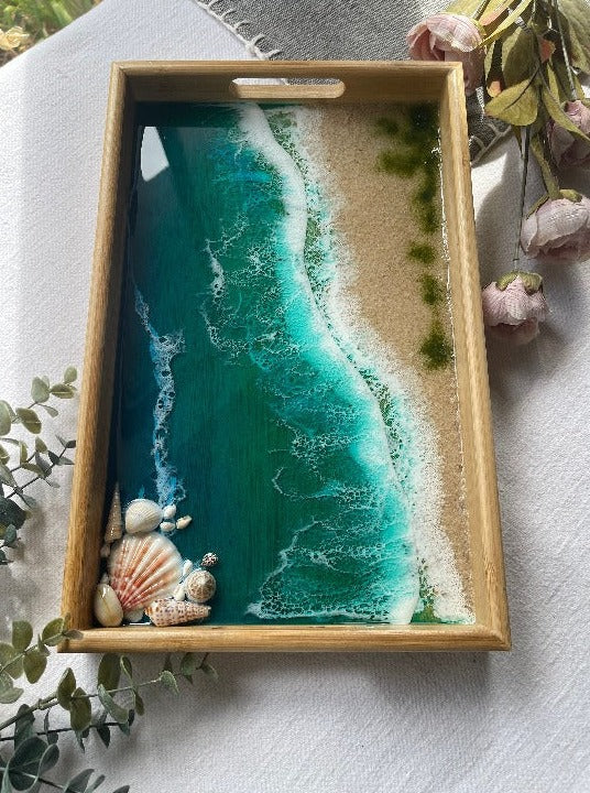 Resin art serving tray featuring a bamboo base, adorned with sea shells and sand, encapsulated in ocean wave designs created with resin.