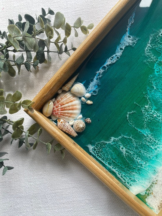 Resin art serving tray featuring a bamboo base, adorned with sea shells and sand, encapsulated in ocean wave designs created with resin.