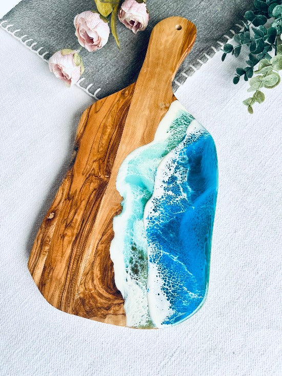 Olive charcuterie board with handle featuring captivating ocean wave resin art - a harmonious blead of nature and epoxy art.