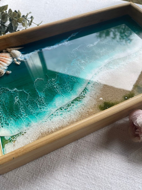 Resin art serving tray featuring a bamboo base, adorned with sea shells and sand, encapsulated in ocean wave designs created with resin.