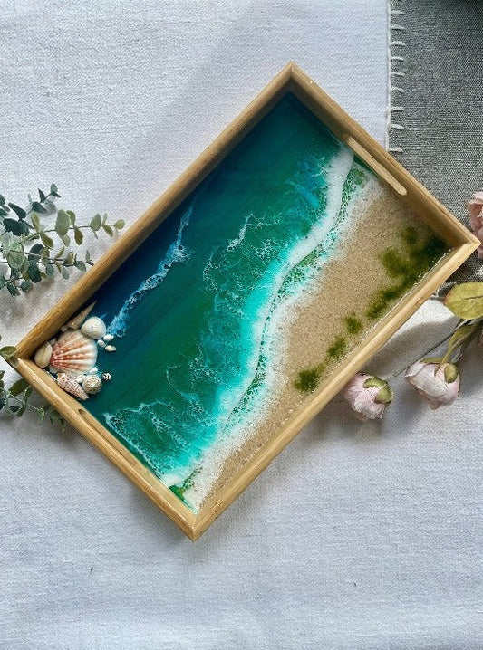 Resin art serving tray featuring a bamboo base, adorned with sea shells and sand, encapsulated in ocean wave designs created with resin. 