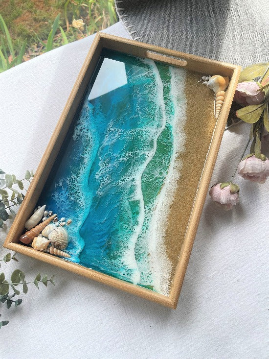 Resin art serving tray featuring a bamboo base, adorned with sea shells and sand, encapsulated in ocean wave designs created with resin.