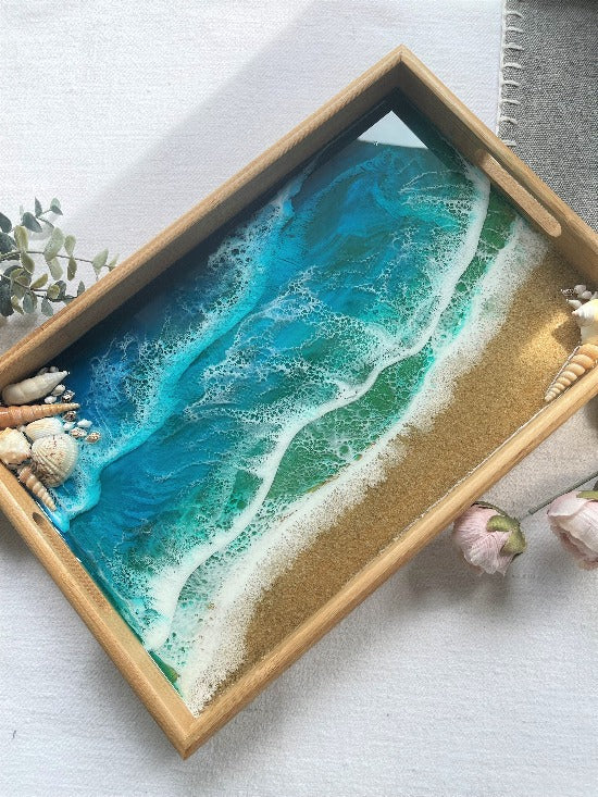 Resin art serving tray featuring a bamboo base, adorned with sea shells and sand, encapsulated in ocean wave designs created with resin.