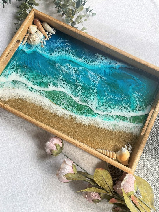 Resin art serving tray featuring a bamboo base, adorned with sea shells and sand, encapsulated in ocean wave designs created with resin.