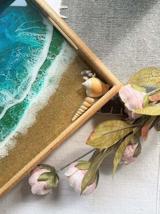 Resin art serving tray featuring a bamboo base, adorned with sea shells and sand, encapsulated in ocean wave designs created with resin.