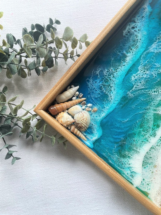 Resin art serving tray featuring a bamboo base, adorned with sea shells and sand, encapsulated in ocean wave designs created with resin.