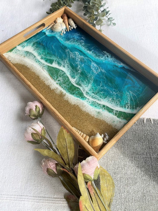 Resin art serving tray featuring a bamboo base, adorned with sea shells and sand, encapsulated in ocean wave designs created with resin.