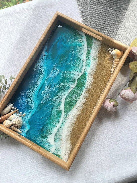 Resin art serving tray featuring a bamboo base, adorned with sea shells and sand, encapsulated in ocean wave designs created with resin.