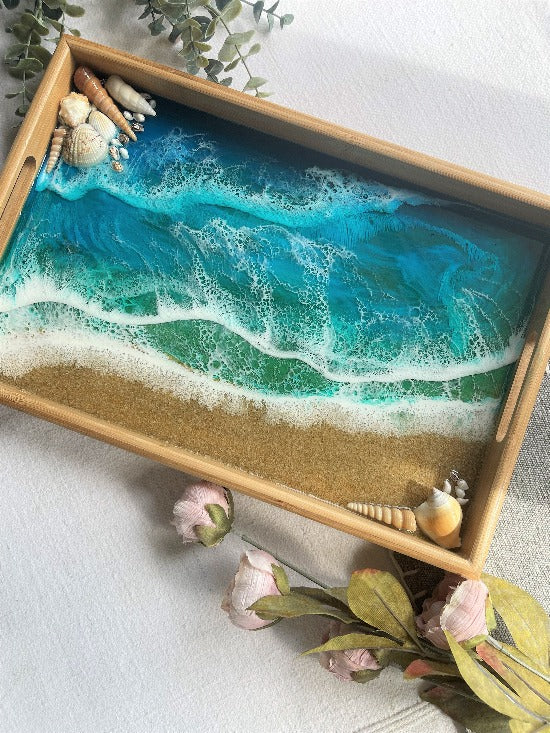 Resin art serving tray featuring a bamboo base, adorned with sea shells and sand, encapsulated in ocean wave designs created with resin.