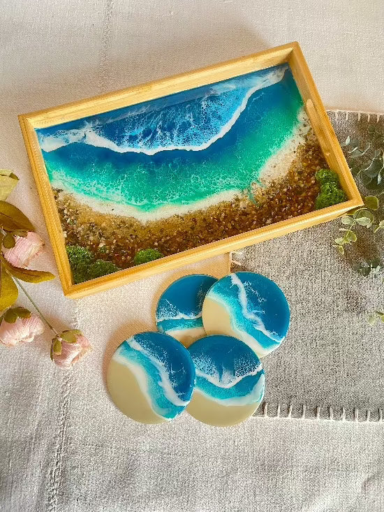 Resin art serving tray featuring a bamboo base, adorned with sea shells and sand, encapsulated in ocean wave designs created with resin. Includes a round set of 4 coasters with waves.