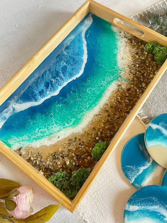 Resin art serving tray featuring a bamboo base, adorned with sea shells and sand, encapsulated in ocean wave designs created with resin. Includes a round set of 4 coasters with waves.