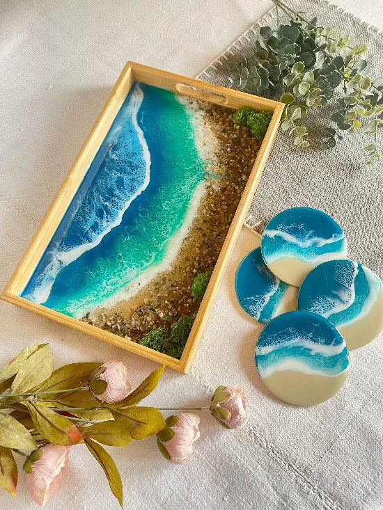 Resin art serving tray featuring a bamboo base, adorned with sea shells and sand, encapsulated in ocean wave designs created with resin. Includes a round set of 4 coasters with waves.