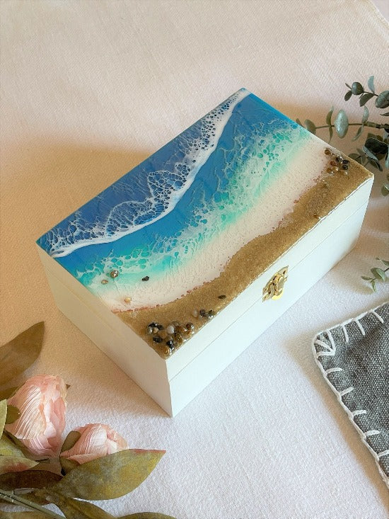 Hand-painted wooden box adorned with resin art depicting ocean waves, seashells, and sand, a unique and artistic product.