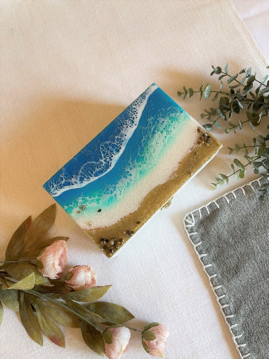 Hand-painted wooden box adorned with resin art depicting ocean waves, seashells, and sand, a unique and artistic product.