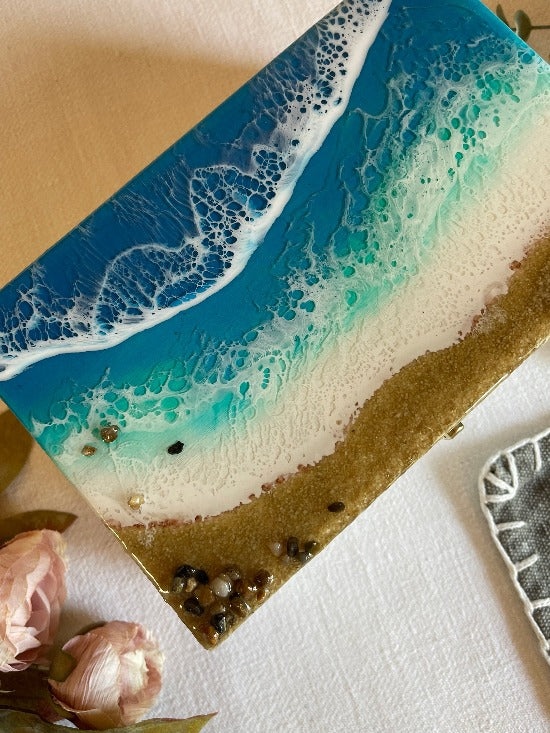 Hand-painted wooden box adorned with resin art depicting ocean waves, seashells, and sand, a unique and artistic product.