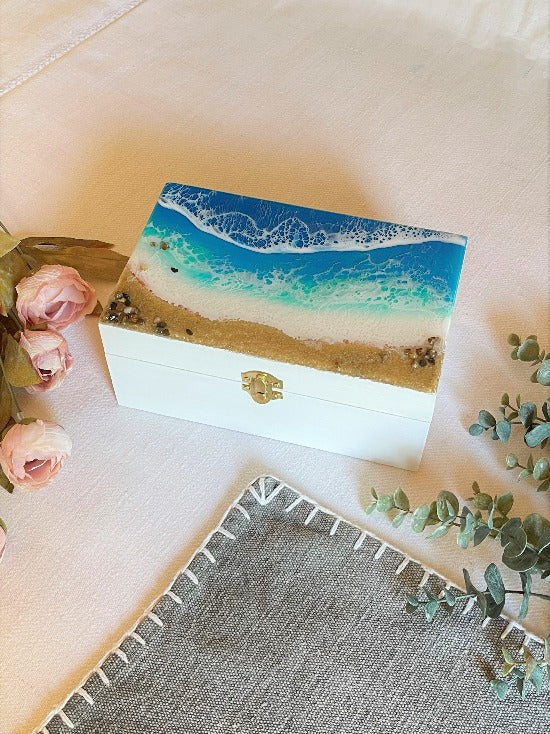 Hand-painted wooden box adorned with resin art depicting ocean waves, seashells, and sand, a unique and artistic product.