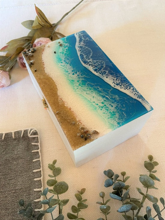 Hand-painted wooden box adorned with resin art depicting ocean waves, seashells, and sand, a unique and artistic product.