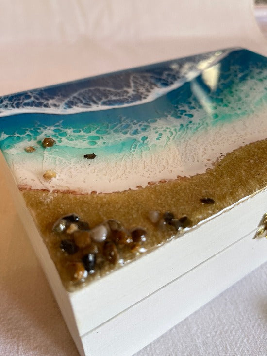 Hand-painted wooden box adorned with resin art depicting ocean waves, seashells, and sand, a unique and artistic product.