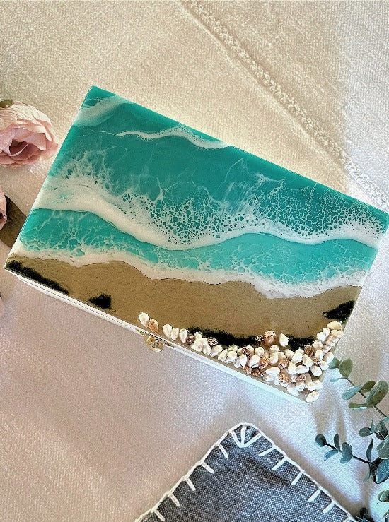 Hand-painted wooden box adorned with resin art depicting ocean waves, seashells, and sand, a unique and artistic product.