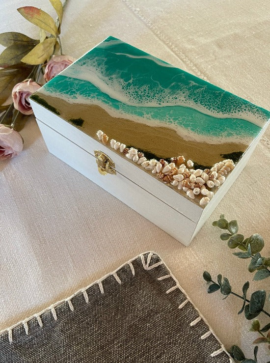 Hand-painted wooden box adorned with resin art depicting ocean waves, seashells, and sand, a unique and artistic product.