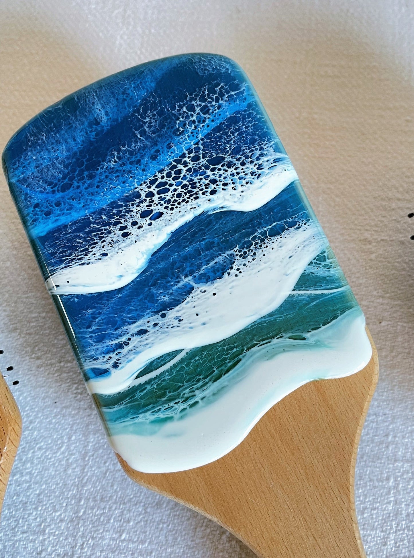 Handcrafted hairbrush featuring resin art with swirling ocean waves design.