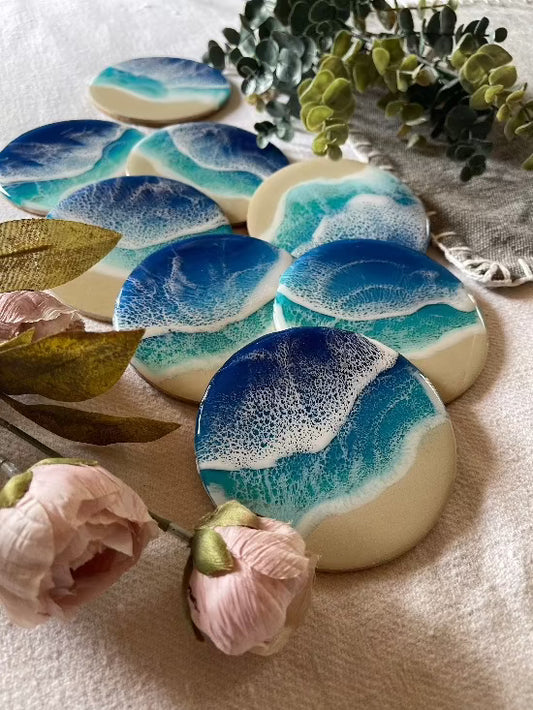 Round resin art coasters featuring a blue color palette with sand and ocean waves design.