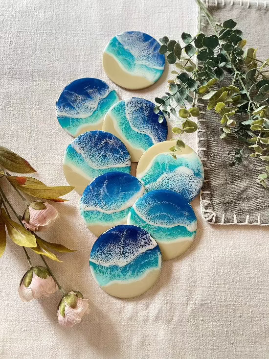 Round resin art coasters featuring a blue color palette with sand and ocean waves design.